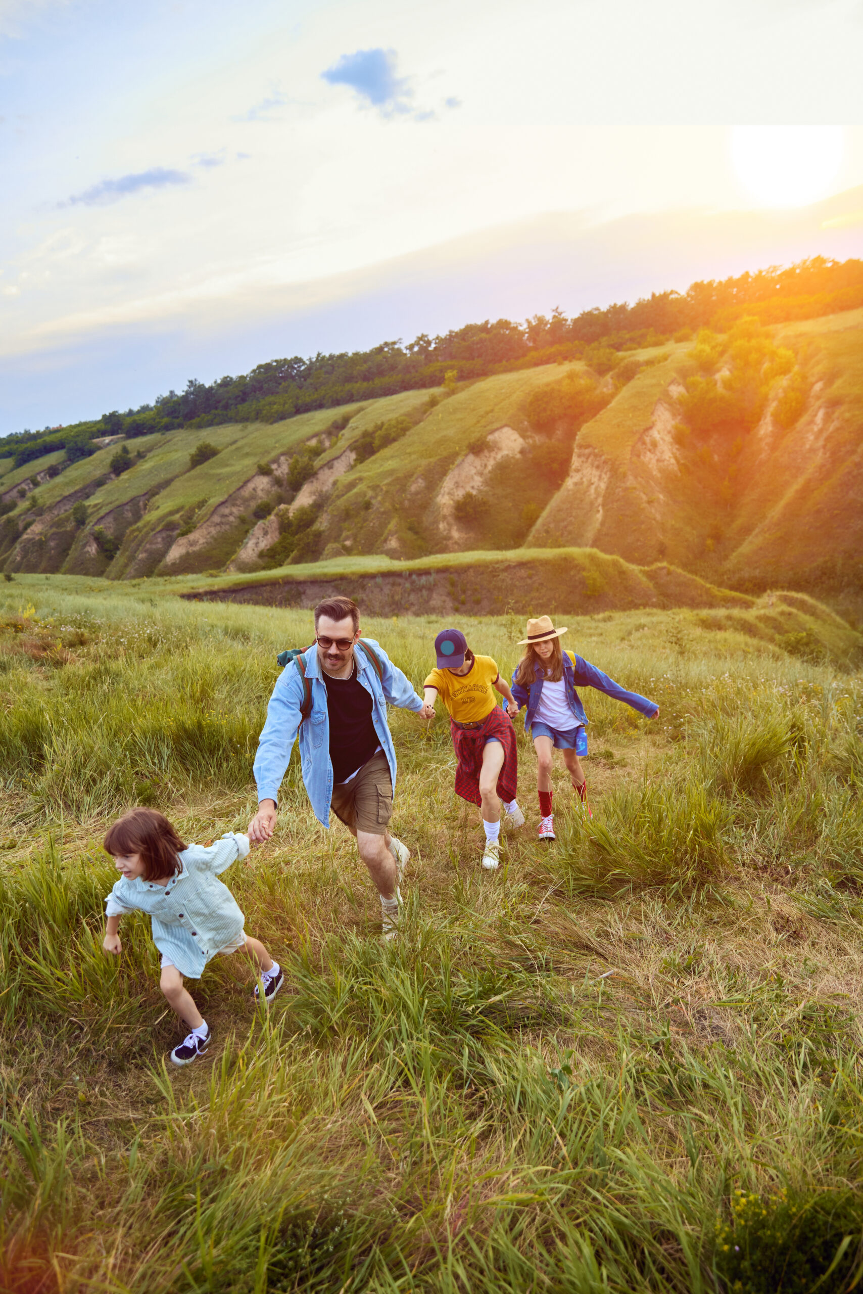 Parents going hiking with their children, daughters on warm summer evening. Beautiful hills landscape. Sunset. Concept of leisure time, fun, nature, active lifestyle, family, travel