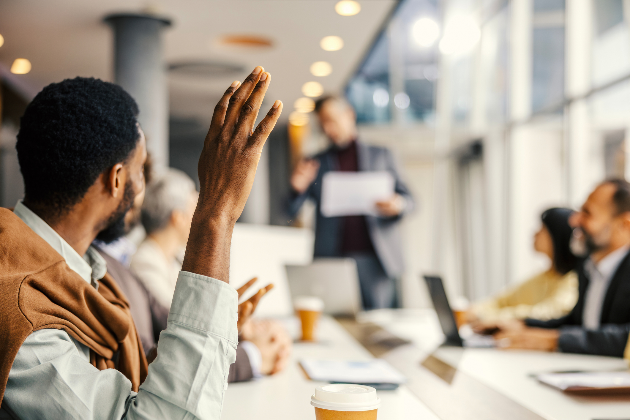 Diverse business professionals attending a corporate presentation, with one man raising his hand, actively engaging and asking questions in the modern conference room